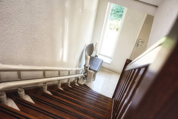 A stairlift, supporting home mobility, is installed on the side of a wooden staircase leading down to a bright entrance hallway with a door and window—ideal for those exploring Grants for Stairlifts UK.
