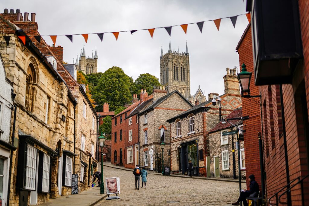 A cobblestone street in one of the Areas Covered is lined with historic buildings leading uphill toward a large cathedral, with stringed flags overhead and a few people walking.