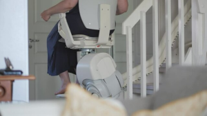 A person sits on a stairlift chair going up a staircase in a home, highlighting an easy way to rent stairlift solutions for enhanced mobility. Part of their upper body and legs are visible.