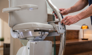 A person operates a stairlift chair installed next to a wooden staircase in a modern home, following advice from a stairlift guide to choose the best model from top stairlift manufacturers.